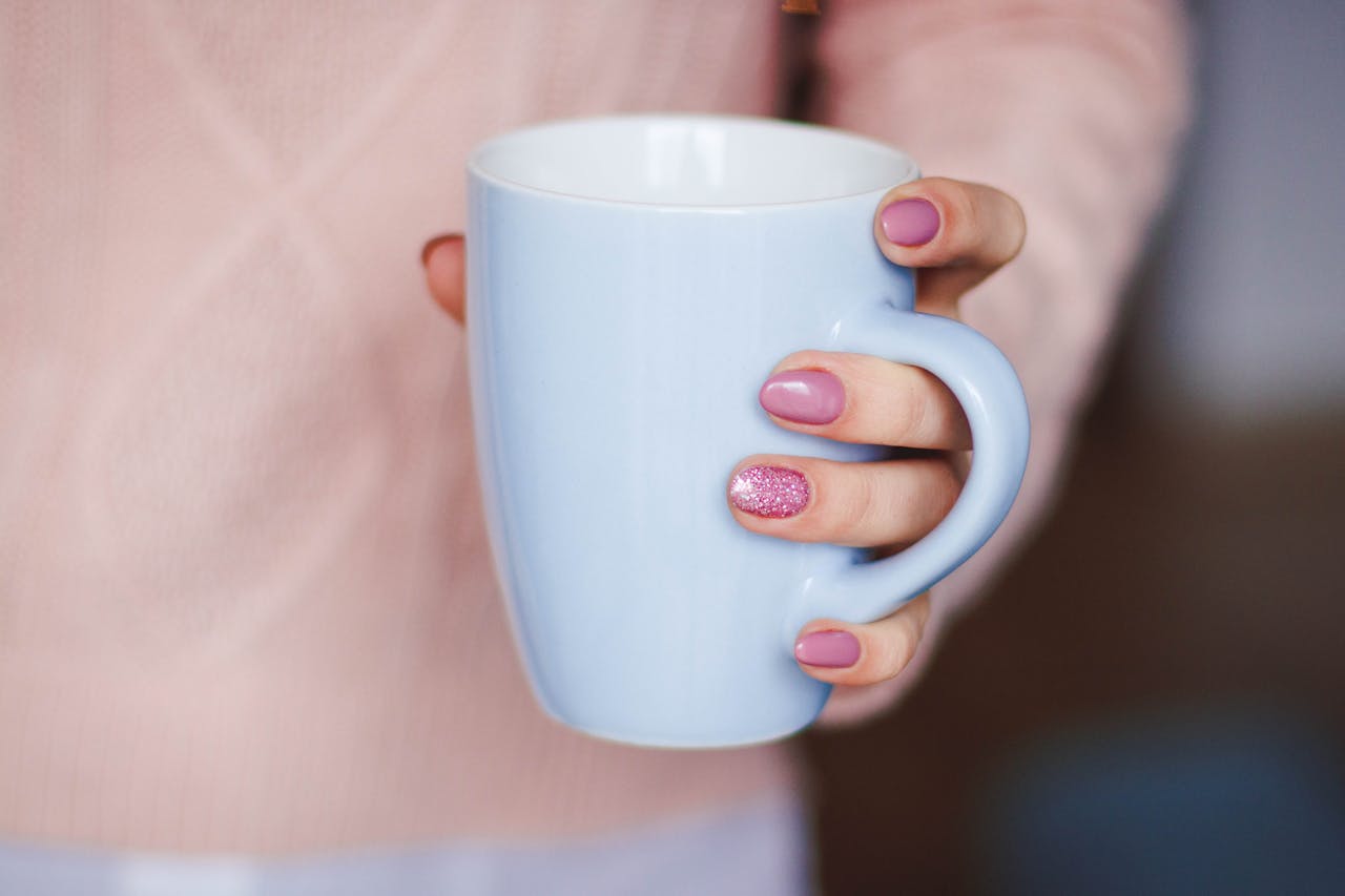 A woman's hand with pink nails holding a light blue mug, indoors.
